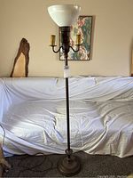 Full view of vintage metal floor lamp with milk glass torchiere shade and two candle-style bulb holders, standing in front of couch.