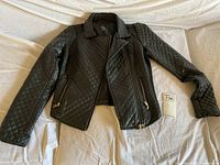 Black quilted leather-like motorcycle jacket laid flat showing front and zippered pockets