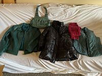 Overview of all outerwear items including teal green leather jackets, black puffer jacket, teal green handbag, and a red scarf laid out on a surface.