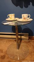 Full view of round glass pedestal table with two character mugs and plates arranged on top