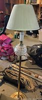Full view of the floor lamp showing the brass base, slender stand, clear cut glass decorative globe in the center, and white pleated lampshade on top.