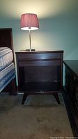 Front view of dark wood nightstand next to bed and dresser, showing overall shape and condition