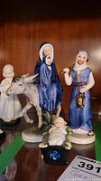 Three Goebel nativity figurines displayed together showing Mary on donkey, Joseph with lantern, and Baby Jesus in manger.