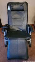Front view of black vegan leather massage chair with head cushion and remote control resting on armrest.