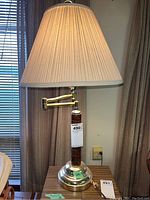 Full view of the table lamp showing beige pleated shade, brass base, and carved wood column with adjustable arm.