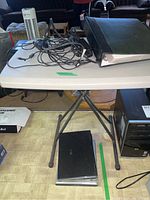 Top view of folding table with charging cords and photo album binder on it with one laptop underneath the table.