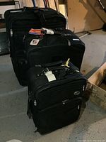Photo showing all three black soft shell suitcases arranged in a row, highlighting the various sizes and attached tags.