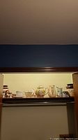 Shelf showing collection including porcelain pitchers with floral design, snowman teapot and matching cream and sugar bowls, and other ceramic items.