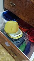 Drawer filled with stacked Pyrex glass dishes and lids, yellow enameled colander on top