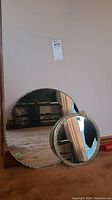 Full view of both round mirrors side by side on floor against wall, showing the difference in size and frame styles.