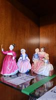 Group photo of three Royal Doulton figurines shown on glass shelf, including Dinky Do, Vanity, and The Bedtime Story.