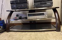 Wooden stand with curved dark wood legs, glass top and two lower shelves holding stereo equipment (not included).