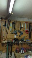 Wide view of pegboard with various hand tools including saws, clamps, levels, and crowbars hanging, some tools placed on shelves below.