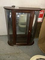 Front view of wood floating curio cabinet with glass doors showing the curved glass sides and door with brass knob.