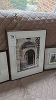 View of three framed pictures leaning on a cushioned bench, showing an arched doorway, bridge print, with label on the largest frame.