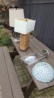 Four different lamps and lamp components arranged on an outdoor bench next to a fence, including table lamps and lighting fixtures.