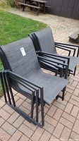 Group of six black outdoor patio chairs with mesh seating and backs, stacked in pairs and placed on a patio.