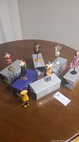 Seven fashion figurines displayed on their stand bases, placed on several rectangular boxes.
