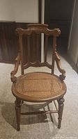 Front view of antique wooden chair showing carved backrest and cane seat