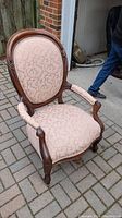 Full view of antique armchair showing carved wooden frame and pink floral upholstery on backrest, seat, and armrests.