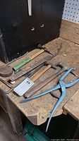 Photo showing various auto body tools including hammers, mallet, dolly, pick tool and pliers on a wooden workbench.
