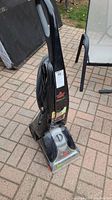 Front angled view of the Bissell ProHeat carpet cleaner showing power cord wrapped on back, label with lot info and black body with clear section at base.