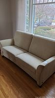 Full view of beige couch showing upholstery and wooden floor base.