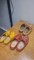 Three pairs of Dutch wooden shoes on a wooden surface, showing the varied paint and design on each pair.