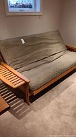 Front view of futon in upright position showing wood frame, slatted arms, and green mattress