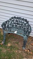 Front angle view of the green iron garden bench showing the ornate grapevine and floral design on the backrest and intricate scrollwork pattern on the seat.