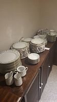 Wide view of stacked fine china plates and cups, creamers on wooden cabinet.