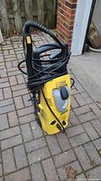 Left-side front view of pressure washer showing yellow body, black handle and hose wrapped on top.