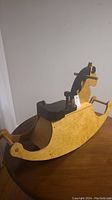Side view of the yellow handmade wooden rocking horse showing the black mane, seat, and curved rocker base.