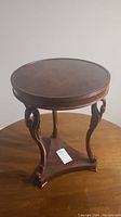 Full view of small round wooden table on a triangular base with carved legs.