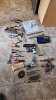 Overview of tool set laid out on floor showing various hand and power tools including pliers, files, wrenches, saws, rotary tool, paint scrapers, drill bits, and others.
