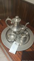 Four-piece Woodbury Pewter set placed on a wooden surface showing the teapot, creamer, sugar bowl, and serving tray.