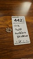 Photo showing the pendant next to a MaxSold lot sticker indicating it is a 10k gold necklace pendant.