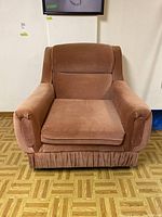 Front view of the brown upholstered armchair showing cushioned seat, back, and skirted base.