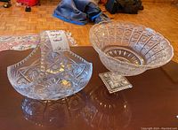 Photo showing the cut glass basket with handle on the left and the cut glass bowl on the right, displayed on a table.