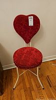Front view of red upholstered bedroom chair with heart-shaped backrest and white metal frame.