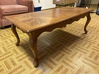 Angled front-left view of wooden coffee table showing carved legs and patterned wood grain top.