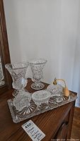 Photo of crystal dresser tray with two crystal vases, three perfume bottles including atomizer, and small ring dish arranged on tray.