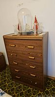 Front view of laminate 5 drawer dresser with wood grain finish and brass handles, two handles damaged.