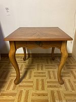 Front view of one wood end table showing square top with decorative grain, curved legs, and drawer with ring pull handle.