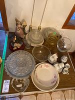 Top view of all items on table showing painted figurines, various glass plates and bowls, pitchers, and mixed china with espresso cups and saucers.