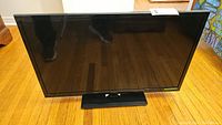 Front view of the Insignia flatscreen TV on hardwood floor, showing screen and base stand.