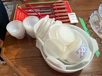 Glass bakeware set including multiple round white opaque glass dishes with blue and red floral pattern and matching lids, shown stacked inside each other.