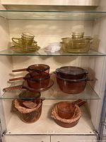 Front view of amber and clear glass cookware and bakeware of various sizes, stacked and nested, including casseroles, saucepans, and bowls.