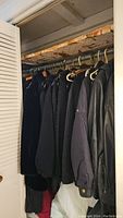 Closet view showing six dark coats hanging on hangers including leather coats.
