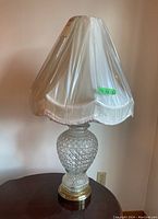 Full view of a table lamp showing fabric shade with plastic cover and glass base on a metal stand.